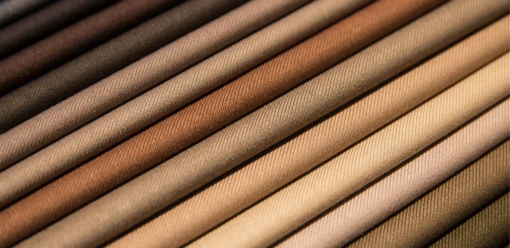 Nahaufnahme von diagonal angeordneten Stoffrollen in verschiedenen Braun-, Beige- und Brauntönen.