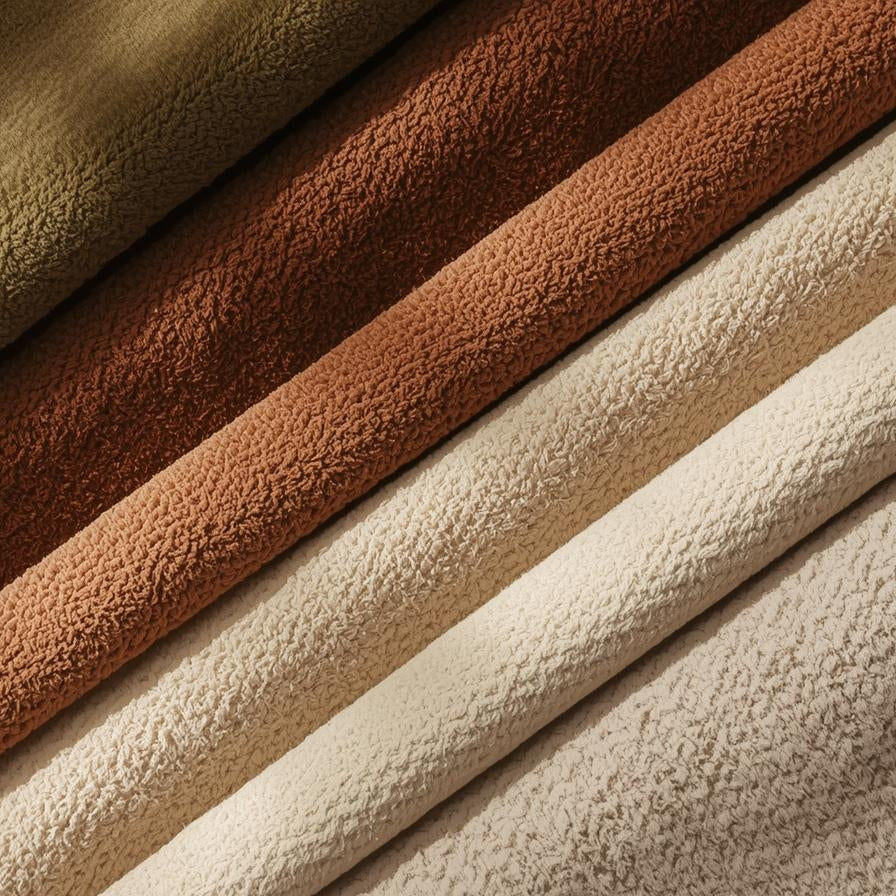 Gefaltete Handtücher in erdigen Braun-, Hellbraun- und Cremetönen, die in diagonalen Reihen angeordnet sind.